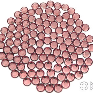 May include: A large quantity of small, round, rose-colored rhinestones. The rhinestones are arranged in a circular pattern on a white background.