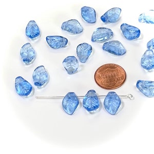 May include: A scattering of light blue glass beads shaped like leaves, with a few beads strung on a wire. A US penny is included for scale.