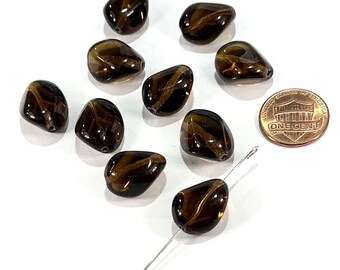May include: A collection of ten polished, brown tiger eye gemstone beads with a golden stripe pattern. A needle is threaded through one bead. A US one-cent coin is included for size reference. The beads are on a white surface.
