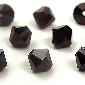 May include: Twelve dark purple faceted glass beads. The beads are cube shaped and have a shiny finish.