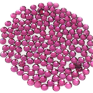 Op de afbeelding: Een grote groep kleine, ronde, roze strass steentjes. De strass steentjes zijn verspreid over een witte achtergrond.