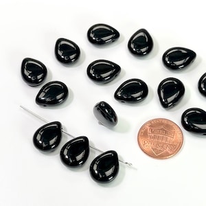 May include: A collection of 14 black teardrop-shaped glass beads. The beads are approximately the size of a US penny.