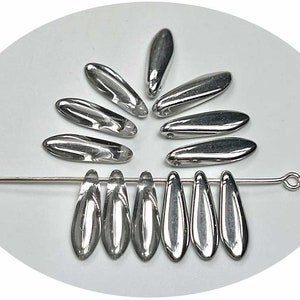 May include: A group of silver-colored glass beads in a teardrop shape. The beads are arranged in a circle and a line. The beads are strung on a wire.