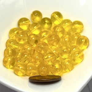 May include: A pile of bright yellow round glass beads in a white bowl. A penny is included for scale.