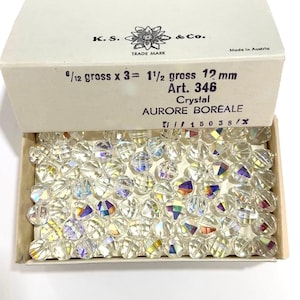 May include: A box of clear glass beads with iridescent rainbow colors. The box is labeled "K.S. & Co. Trade Mark" and "Made in Austria". The beads are 12 mm in size and are labeled "Art. 346 Crystal Aurore Boreale".