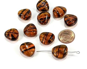 May include: A collection of amber-colored, irregularly shaped glass beads with black stripe designs. A U.S. one-cent coin is included for size reference. The beads are strung on a silver-colored wire, suggesting they are for jewelry making or crafts.