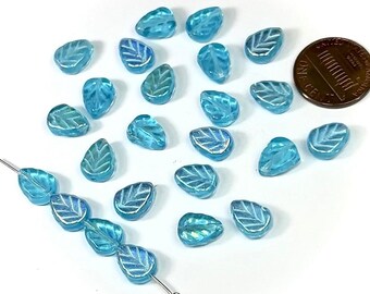 May include: A collection of turquoise blue glass beads in the shape of leaves. The beads have a white leaf design and are strung on a wire.