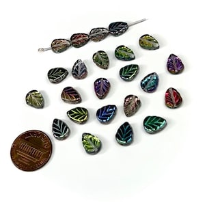 May include: Assortment of iridescent glass leaf beads with a variety of colors, including green, blue, purple, and red. The beads are scattered on a white surface, with a penny for scale.