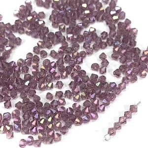 May include: A large quantity of small, iridescent purple glass beads. The beads are faceted and have a pointed shape.