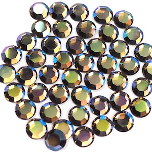 May include: A group of iridescent, round, faceted rhinestones in shades of green, blue, and brown. The rhinestones are scattered on a white background.