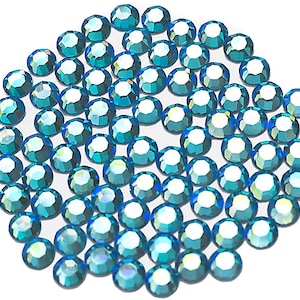 Op de afbeelding: Een grote groep turquoise blauwe strass steentjes, gerangschikt in een cirkelvormig patroon. De strass steentjes zijn gefacetteerd en hebben een glinsterende afwerking.
