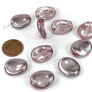 May include: Ten iridescent pink glass beads with a smooth, oval shape. The beads have a subtle shimmer and are approximately the size of a US penny.