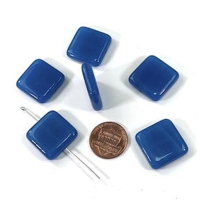 May include: Six square-shaped glass beads in a vibrant blue color. The beads are approximately the size of a US penny.
