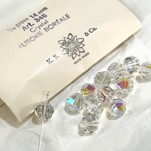 May include: A close-up of a package of 14 mm crystal beads labeled "1/12 gross Art. 346 Crystal Aurore Boreale K.S. & Co. Trade Mark". The beads are clear and have a rainbow iridescent effect.