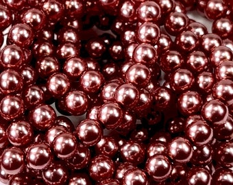 May include: A close-up shot of a pile of shiny, round, dark rose-colored beads. The beads are clustered together, reflecting light and creating a textured surface. These beads are suitable for jewelry making and craft projects.