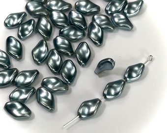 May include: A collection of pearlescent, gray-blue beads scattered on a white surface. The beads have a unique, organic shape, with a smooth, reflective surface. Some beads are strung together, showcasing their potential use in jewelry making.