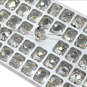 Peut inclure: Gros plan sur une perle en verre transparente avec un design facetté. La perle est sur un plateau blanc avec d'autres perles du même design.