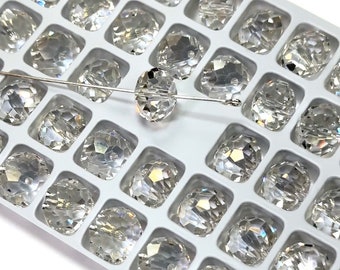 May include: A close-up of a clear glass bead with a faceted design. The bead is on a white tray with other beads of the same design.
