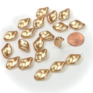 May include: A collection of 18 gold-colored, iridescent, faceted glass beads. The beads are shaped like a teardrop with a flat bottom. The beads are arranged in a circle around a US penny.