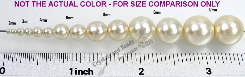 May include: A size comparison of white pearl beads, ranging in size from 2mm to 12mm. The beads are lined up on a white surface with a ruler underneath for reference. The text "NOT THE ACTUAL COLOR - FOR SIZE COMPARISON ONLY" is printed above the beads.