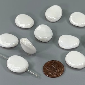 May include: A collection of ten white, oval-shaped ceramic beads with a pearlescent finish. The beads are approximately the size of a US penny.