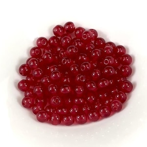 May include: A pile of small, round, red beads. The beads are translucent and have a glossy finish.