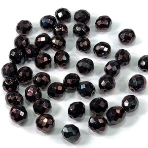 May include: A collection of dark brown faceted glass beads. The beads are oval shaped and have a iridescent finish.