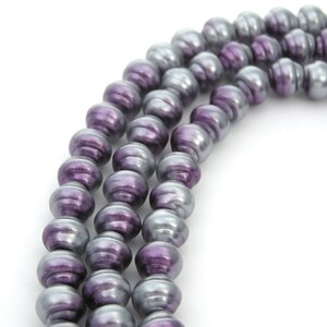 May include: A strand of purple and silver iridescent glass beads. The beads are round and have a smooth, shiny finish.