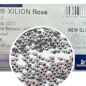 May include: Close-up of a package of 2028 XILION Rose SS 12 Crystal (001) Aurora Boreale (AP) M-Foiled Hotfix 10/00/00 gro. The package features a close-up of the crystals, a barcode, and the Swarovski logo.