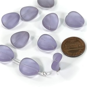 May include: A collection of lavender glass beads in various shapes, including oval and teardrop, with a penny for scale.