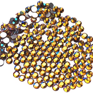 Op de afbeelding: Een grote hoeveelheid kleine, ronde, iriserende amberkleurige strasssteentjes. De strasssteentjes hebben een platte achterkant en een gefacetteerd, reflecterend oppervlak.