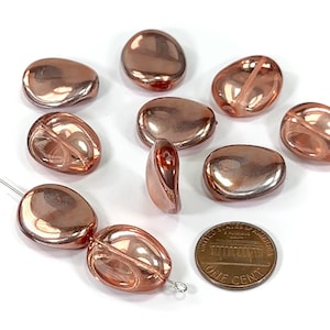 May include: A group of ten rose gold glass beads, some with a clear center, next to a US penny for size comparison.
