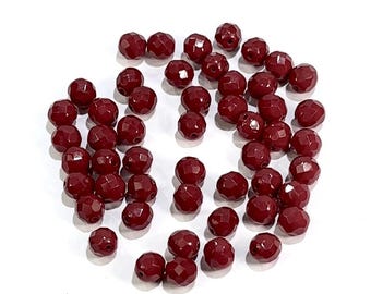 May include: A scattering of dark red faceted glass beads. The beads are round and have a shiny finish.