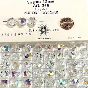 May include: A close-up of a box of 12 mm crystal beads with a rainbow aurora borealis effect. The box is labeled "Art. 346 Crystal Aurore Boréale" and "D.S. & Co. Trade Mark". The beads are displayed in a clear plastic tray.