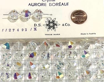 May include: A close-up of a box of 12 mm crystal beads with a rainbow aurora borealis effect. The box is labeled "Art. 346 Crystal Aurore Boréale" and "D.S. & Co. Trade Mark". The beads are displayed in a clear plastic tray.