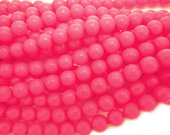 May include: A close-up of a pile of bright pink round beads. The beads are smooth and glossy, and they are arranged in a random pattern.