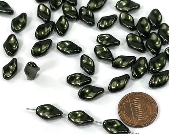 May include: A group of dark green iridescent glass beads in a teardrop shape. The beads are scattered on a white surface with a penny for scale.