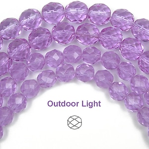 May include: A strand of light purple faceted glass beads. The beads are round and have a shiny finish. The beads are arranged in a semi-circle shape. The image is taken in outdoor light.