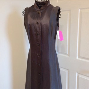 May include: A sleeveless, button-down dress in a dark brown satin-like fabric. The dress has a mandarin collar and a fitted silhouette. A pink tag hangs from the dress. The dress is displayed on a black dress form.