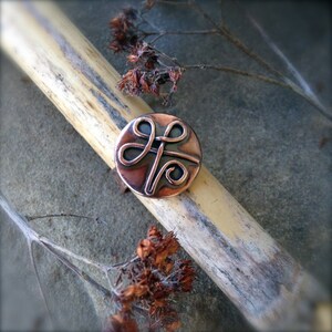 May include: A copper ring with a Celtic knot design. The ring is on a wooden surface.
