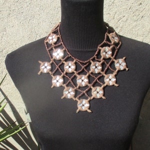 May include: A brown and silver beaded necklace with a geometric design. The necklace is made of small, round beads and features a pattern of interlocking squares.