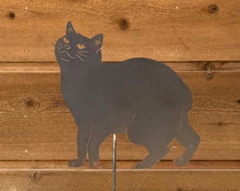 May include: A dark gray metal silhouette of a cat standing in profile, featuring cut-out details for the eyes, nose, mouth, and whiskers. The cat figure is attached to a thin, vertical metal stake extending from the bottom of the body.
