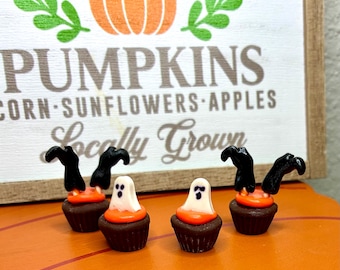 Könnte beinhalten: Vier Miniatur-Cupcake-Figuren mit dunkelbraunen Basen und orangefarbenem Zuckerguss. Zwei Cupcakes sind mit weißen Geisterfiguren verziert, während die anderen beiden schwarze Hexenbeine zeigen, die aus dem orangefarbenen Guss ragen.