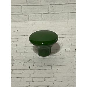 May include: A solid dark green cabinet knob with a smooth, glossy finish. The knob features a rounded, slightly domed top surface that tapers down into a cylindrical base, providing a simple and functional design for furniture or cabinetry hardware.