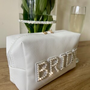 May include: White zippered cosmetic bag with a pearl embellished "BRIDE" design.
