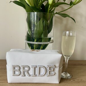 May include: White zippered makeup bag with the word "BRIDE" spelled out in pearl-like embellishments.