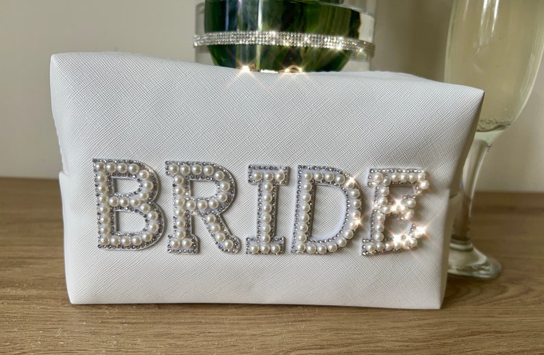 May include: White cosmetic bag with the word "BRIDE" spelled out in faux pearls.