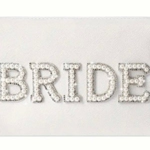 May include: A white cosmetic bag with a zipper closure. The bag has the word "BRIDE" spelled out in pearl-like embellishments.