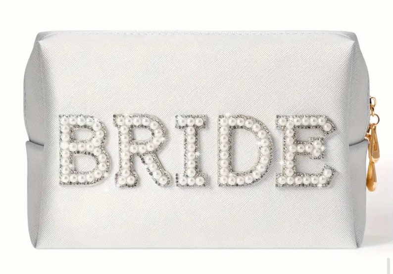 May include: A white cosmetic bag with a zipper closure. The bag has the word "BRIDE" spelled out in pearl-like embellishments.