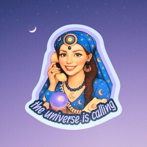 May include: A sticker featuring a smiling woman in a blue headscarf and dress, holding a vintage phone. The text "the universe is calling" is below her. A crystal ball and crescent moon are also visible. The background is a gradient of purple and blue.